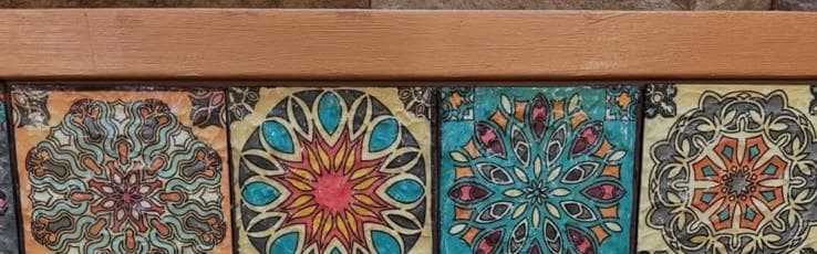 Hand-painted mosaic tiles being laid into a wooden frame